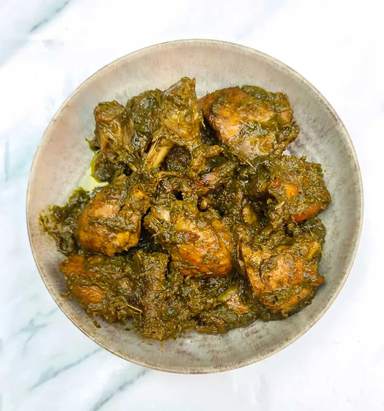 A bowl of cooked cooked green chicken mixed with chunks of curry, served on a white marble surface.